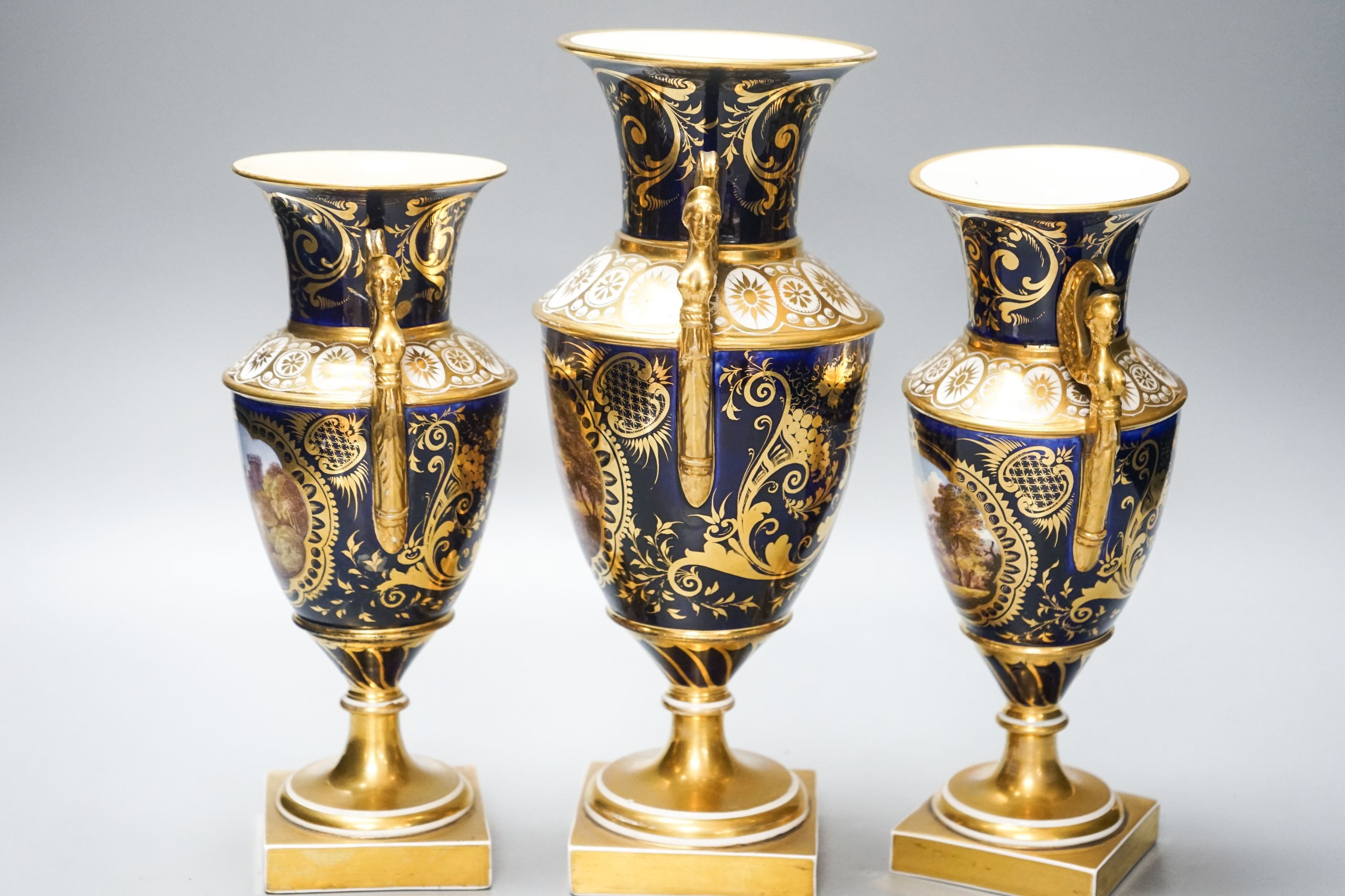 A garniture of three early 19th century English porcelain vases, c.1815-20, each painted with topographical views, tallest 26cm